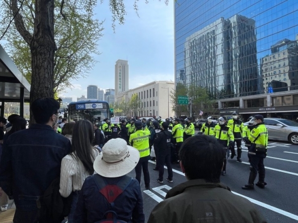 한 활동가가 ‘우리의 미래는 우리가 바꾼다’라는 피켓을 들고 있다. 수십 명의 경찰이 그를 둘러싸고 있다. / 박서윤